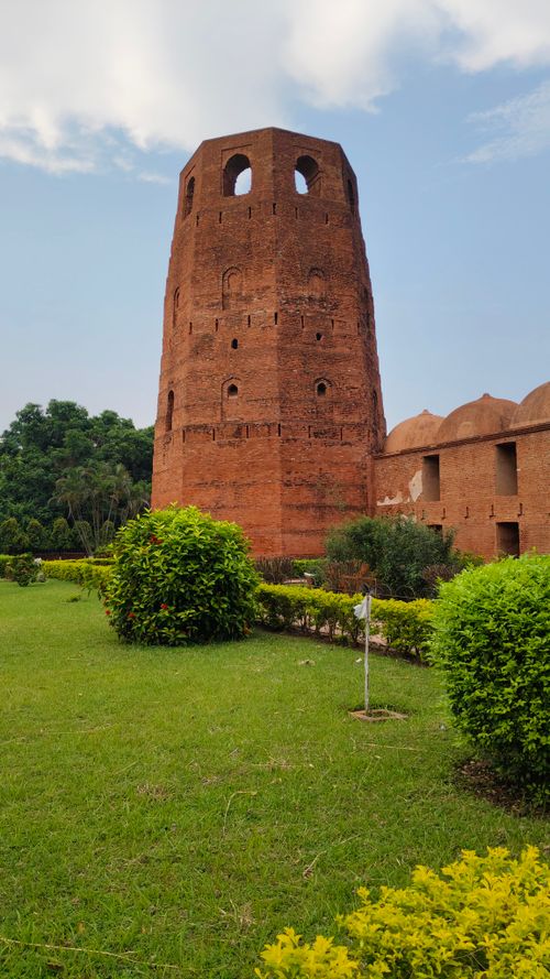 Free Majestic ancient red brick tower surrounded by green foliage under a clear sky. Stock Photo