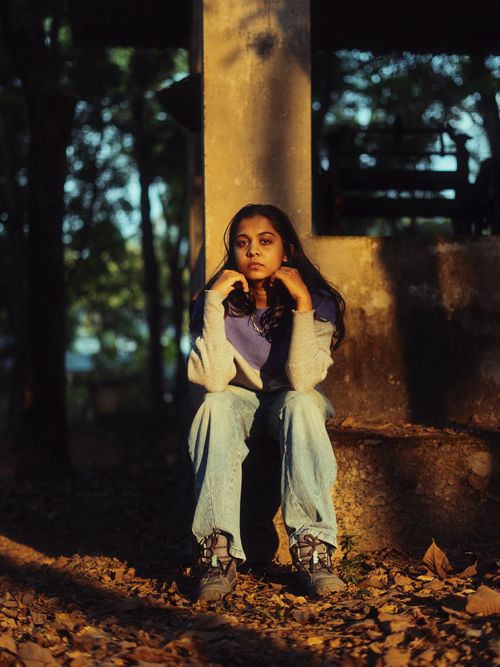 Free Young woman in jeans and sweater sitting outdoors with thoughtful expression, surrounded by autumn leaves. Stock Photo