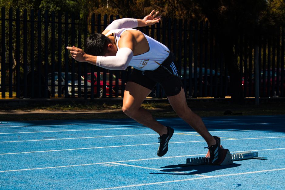 Dynamic shot of an athlete starting a race on a blue outdoor track, showcasing speed and determination. Dynamic shot of an athlete starting a race on a blue outdoor track, showcasing speed and determination.