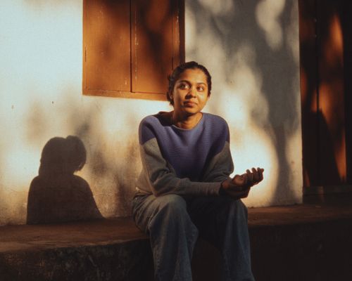 Free A contemplative young woman sits in warm sunlight, casting shadows. Stock Photo