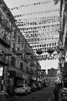 Captivating black and white photo of a Chinatown street with flags and lanterns.