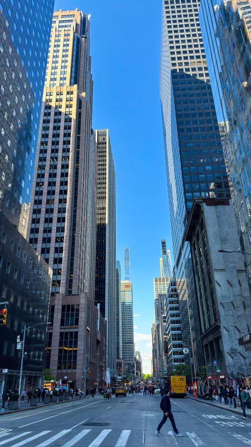 Free Dynamic view of a bustling New York street lined with skyscrapers against a clear blue sky. Stock Photo