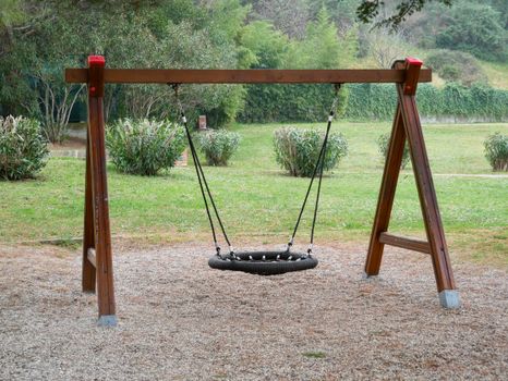 A single swing in a serene park setting with greenery and shrubs.