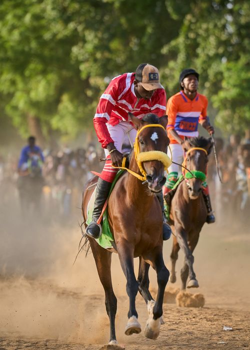 Free Riders compete in a lively horse race on a dusty path in Zaria City, Nigeria. Stock Photo