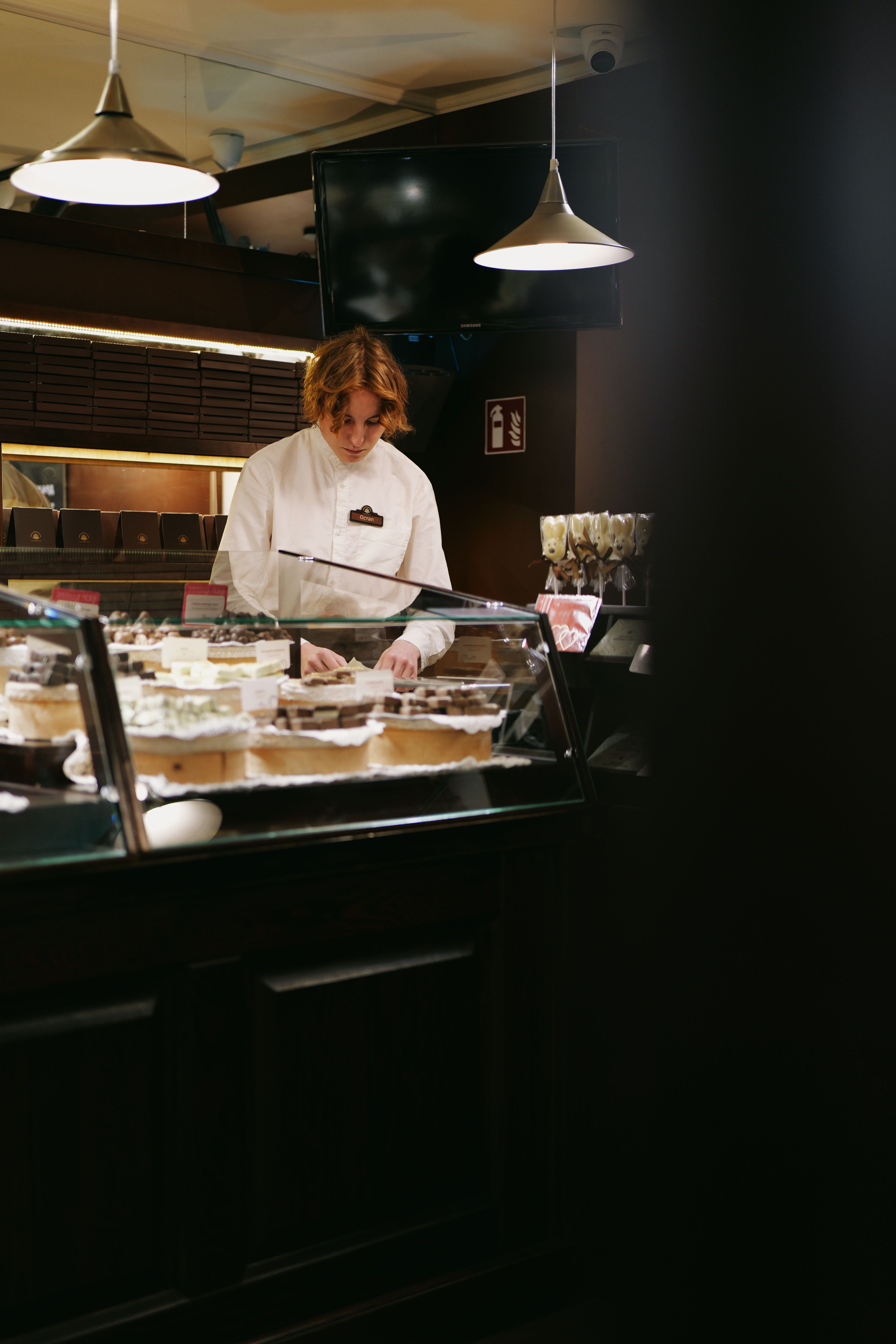 A pastry chef organizes delicious desserts in a cozy Lviv bakery display.