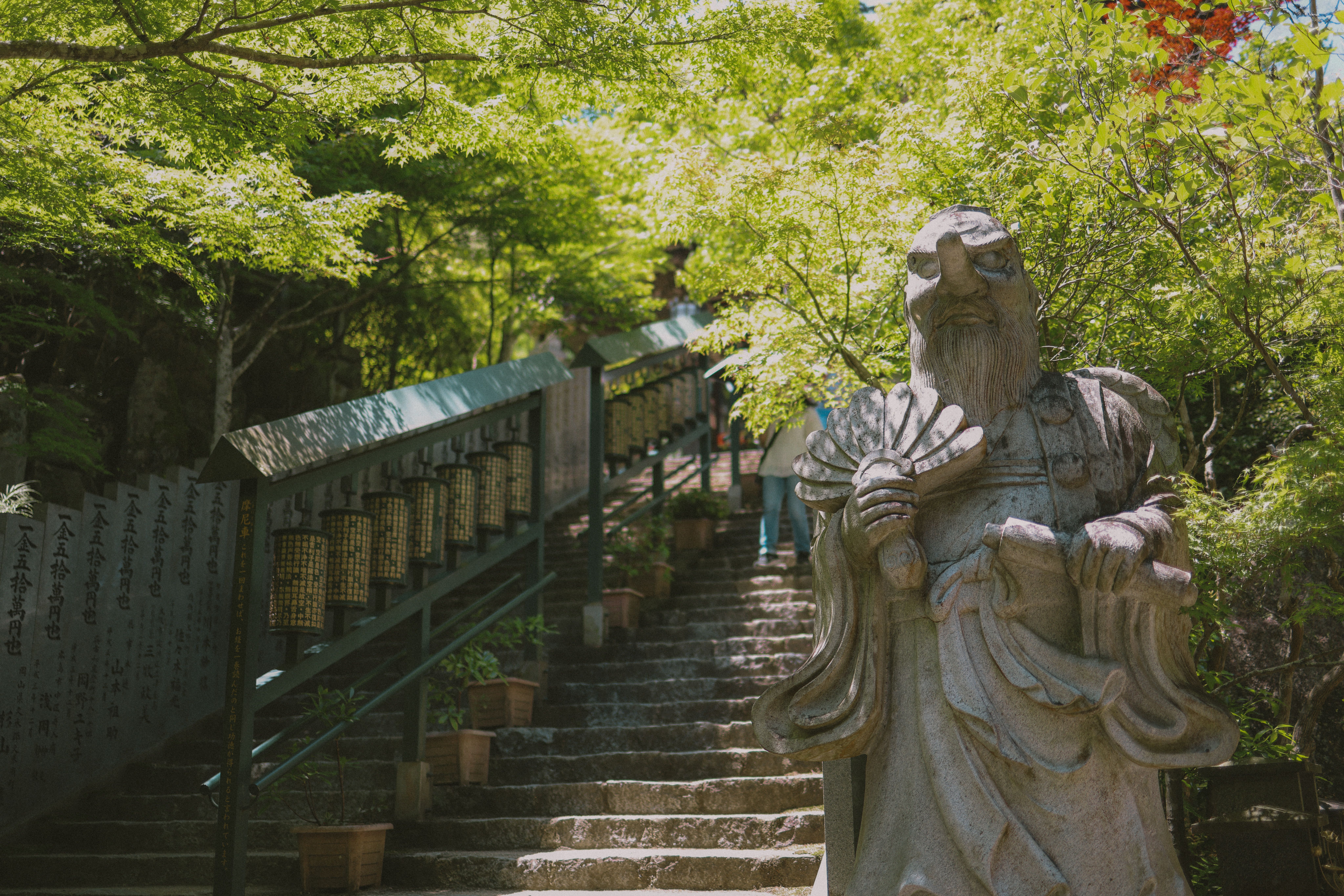Stone statue near lush green staircase in a tranquil outdoor setting with sunlight filtering through leaves.