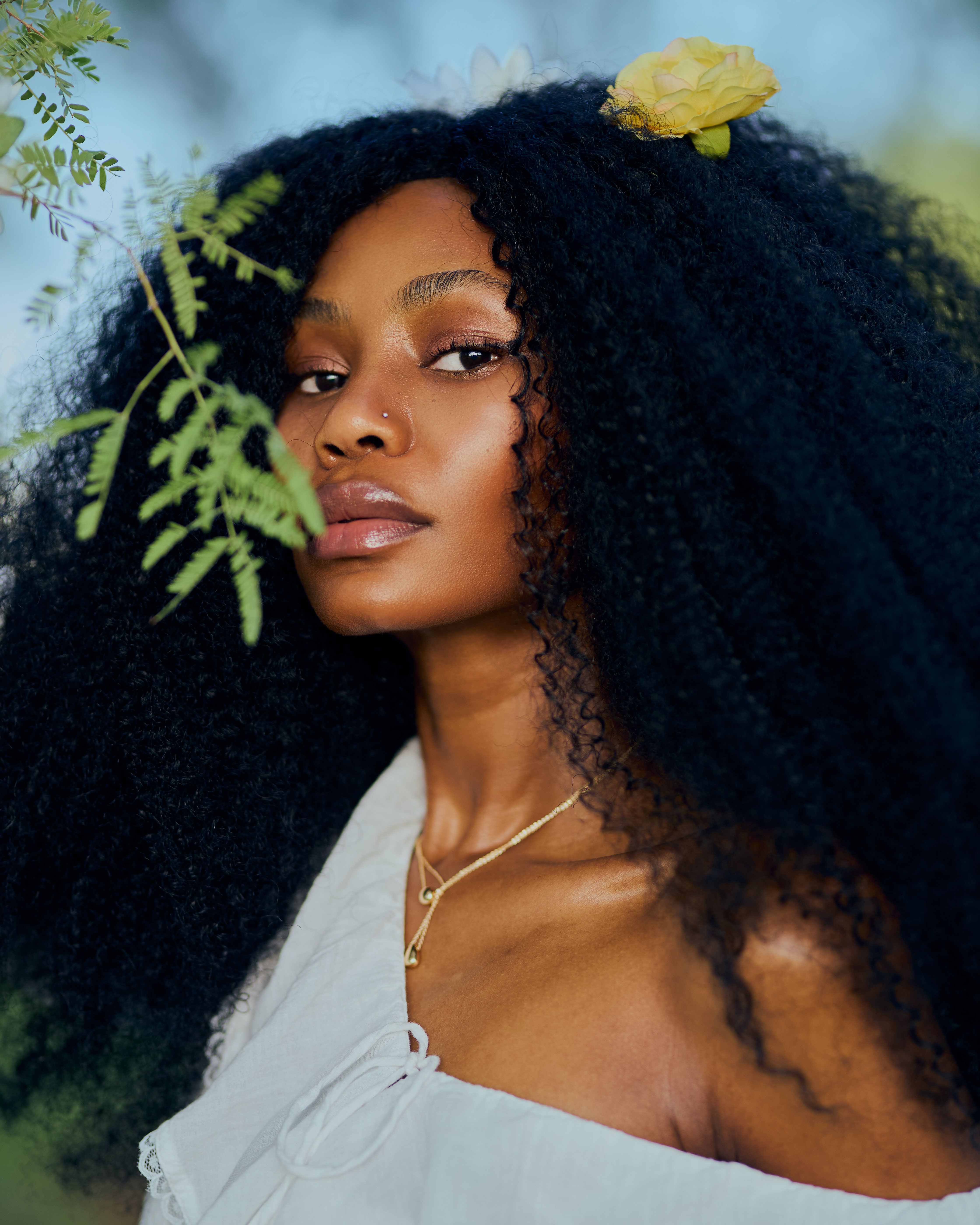 Close-up portrait of an elegant woman with natural afro hairstyle and floral accessory.