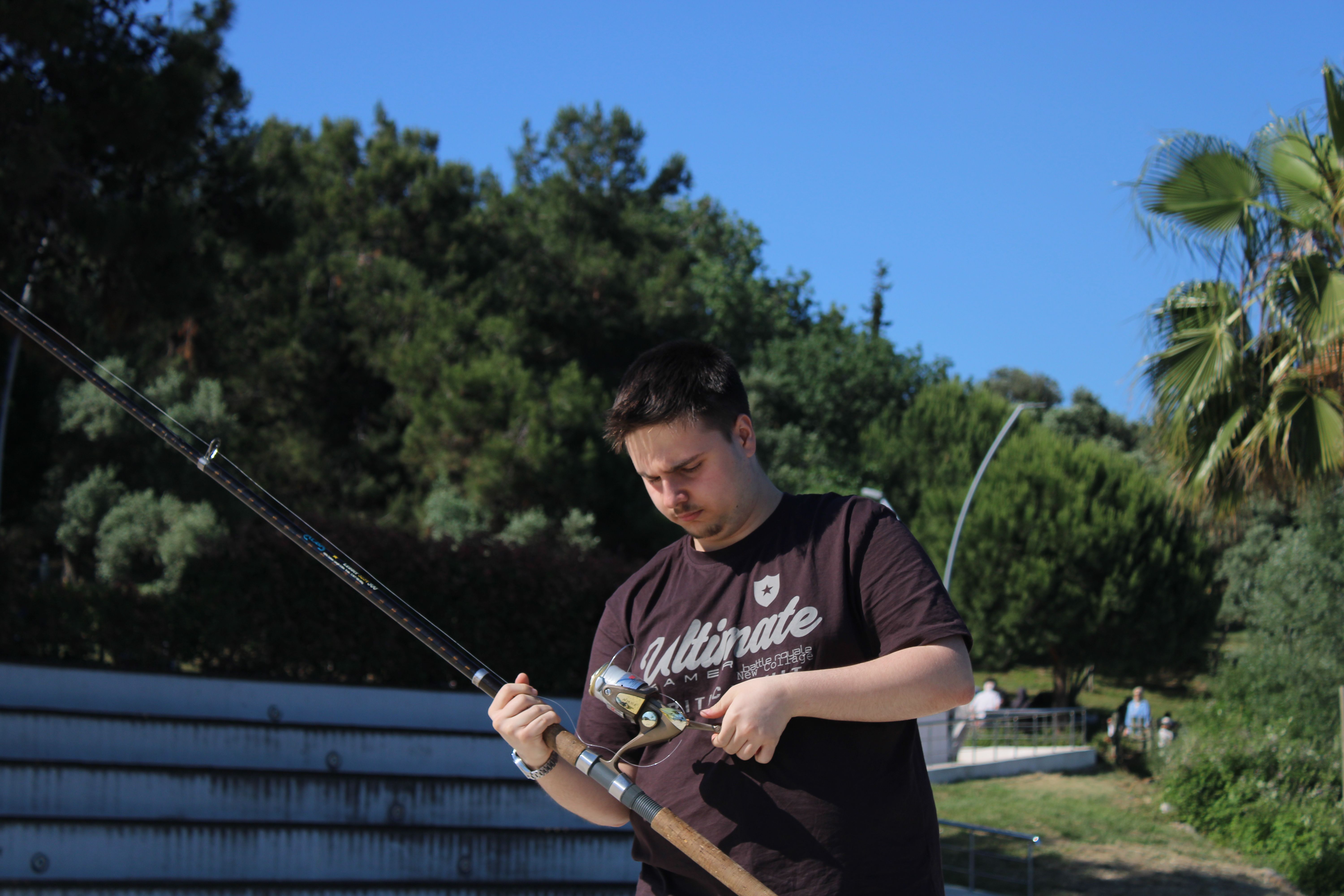Young man setting up a fishing rod in a lush Darıca park, Türkiye.