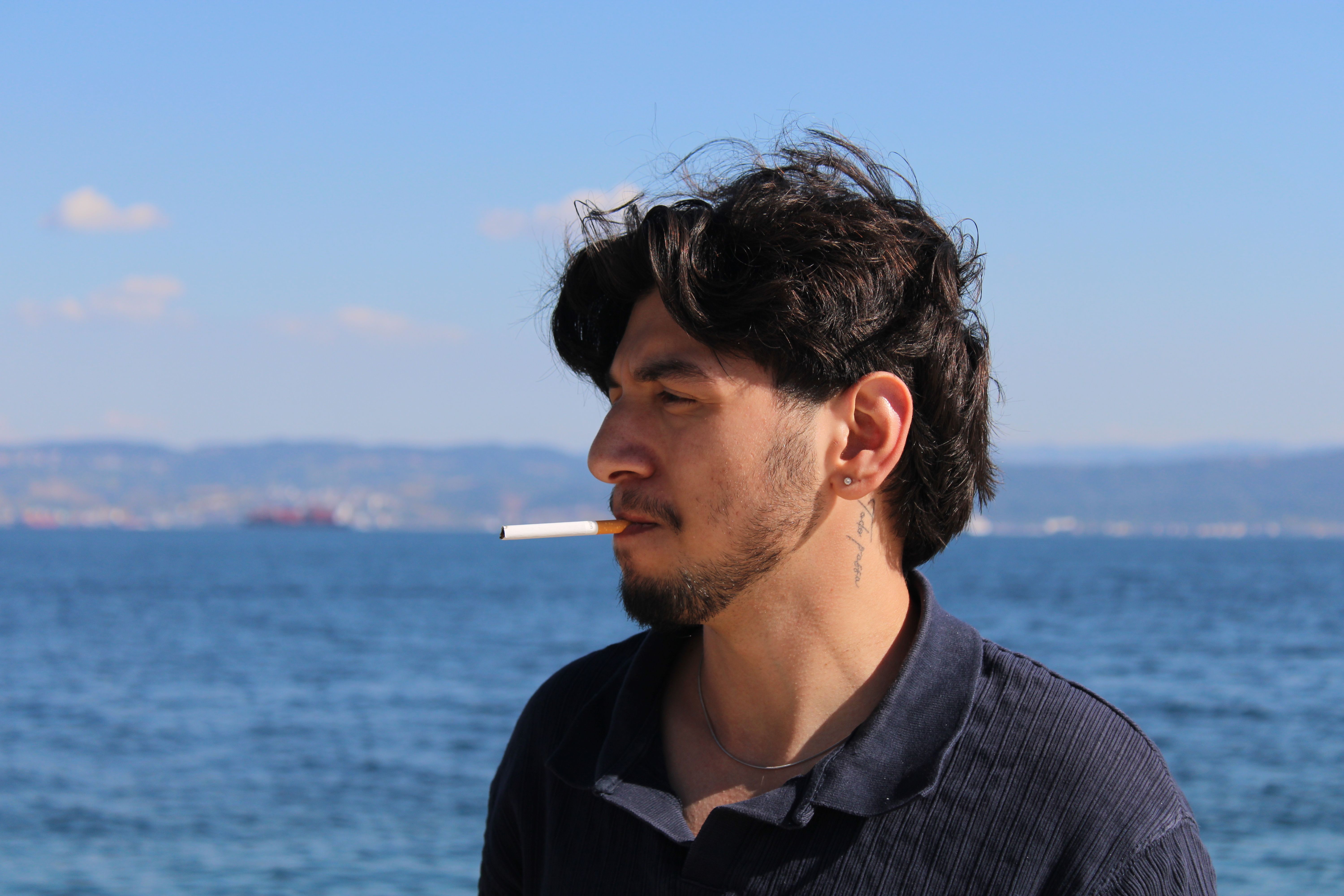 A young man with a cigarette gazes over the sea in Darıca, Türkiye. Captured on a sunny day.