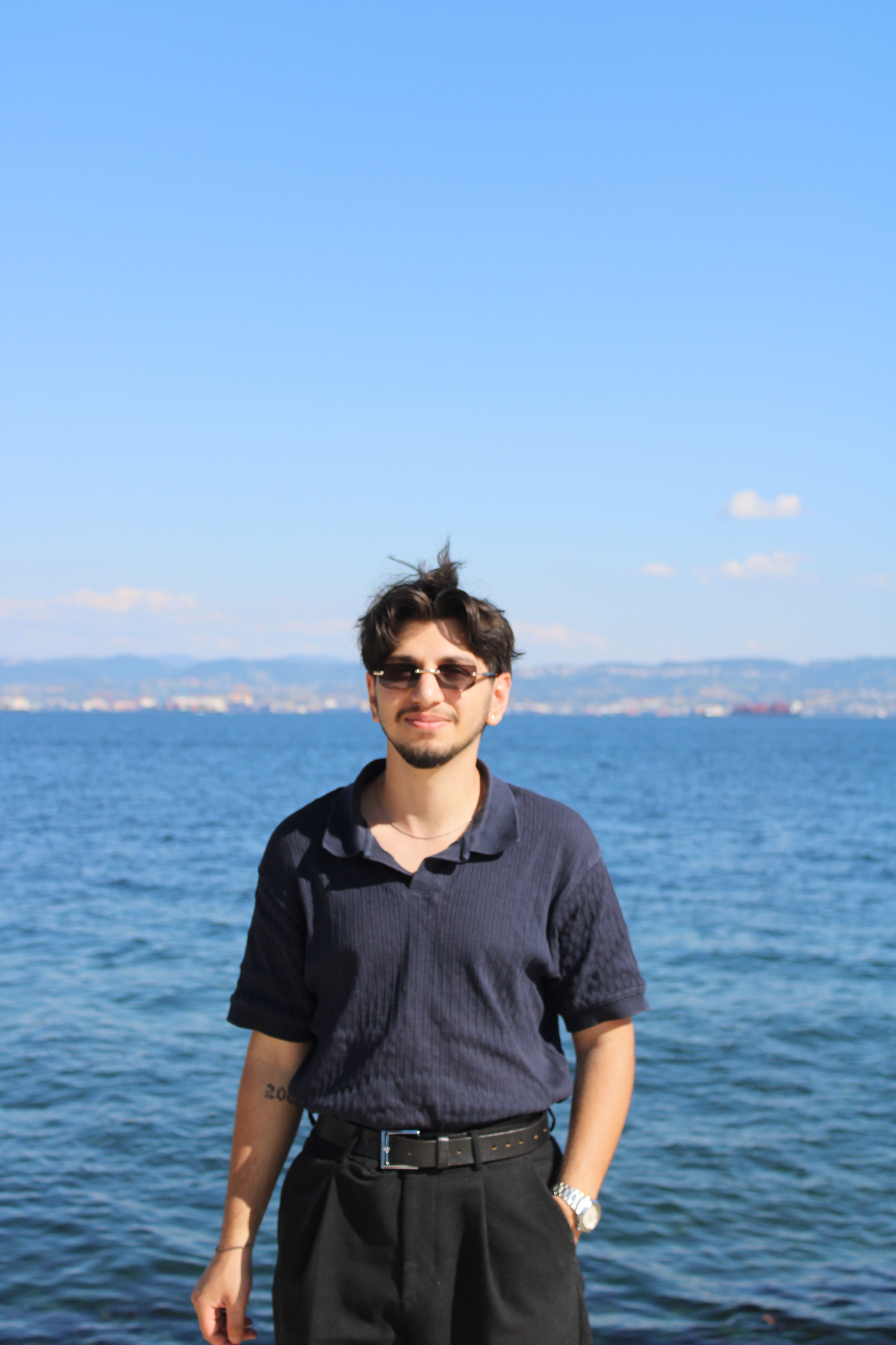 Young man standing by the sea on a sunny day in Darıca, Kocaeli, Türkiye, with a clear blue sky.