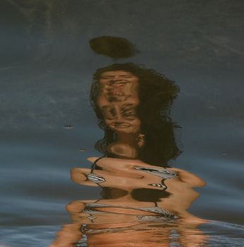 Abstract reflection of a woman in water creates a distorted, artistic visual.