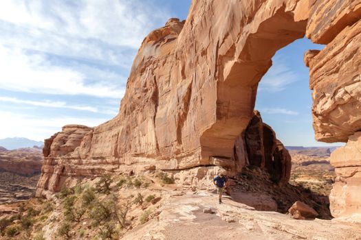 A hiker standing under a massive sandstone arch in Moab's Arches National Park.