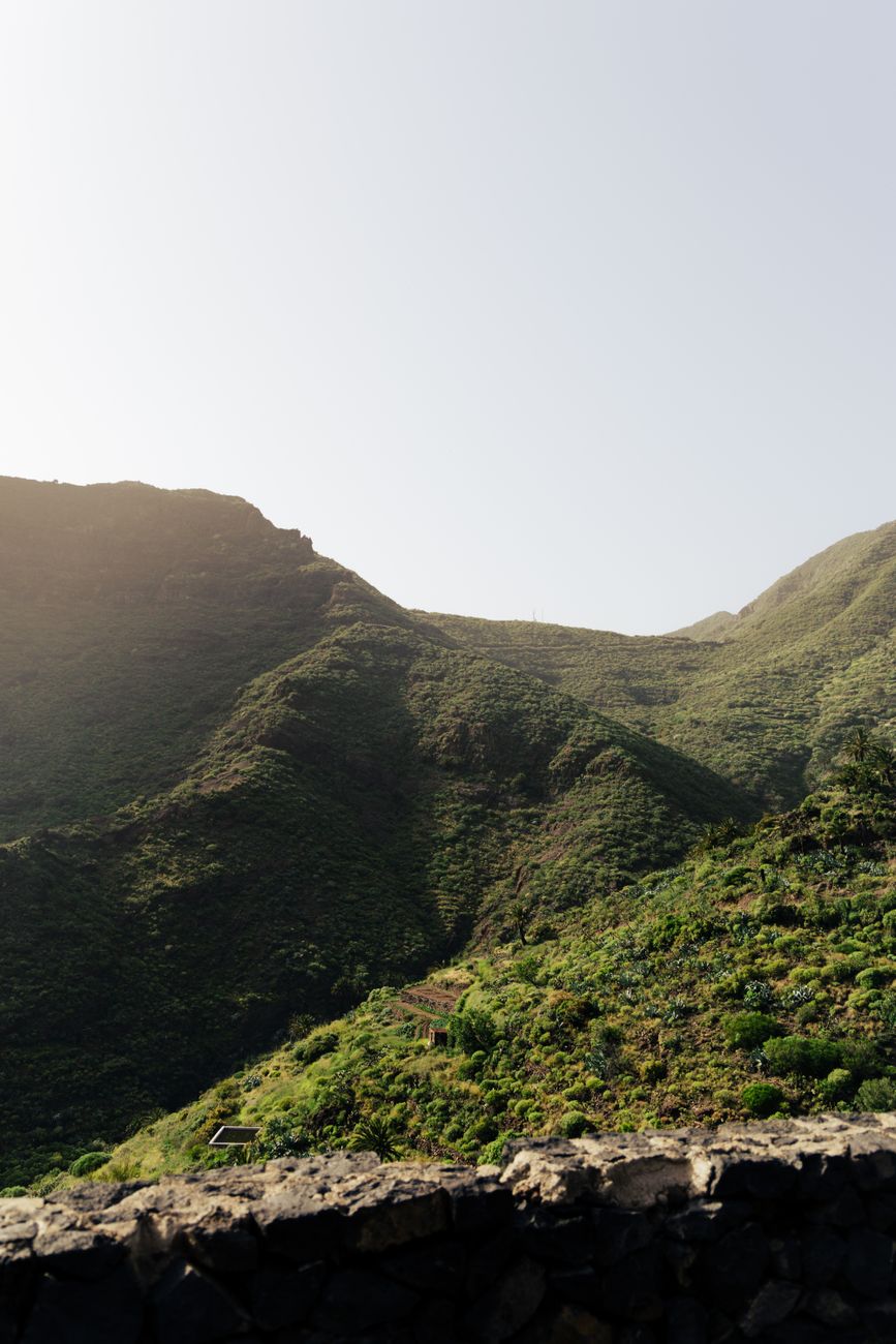 Capture the serene beauty of lush green mountains in Masca Valley, Spain, under clear skies.
