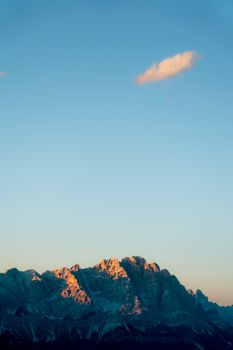 Bright sunrise casting warm hues on mountains in Veneto, Italy, with clear sky.