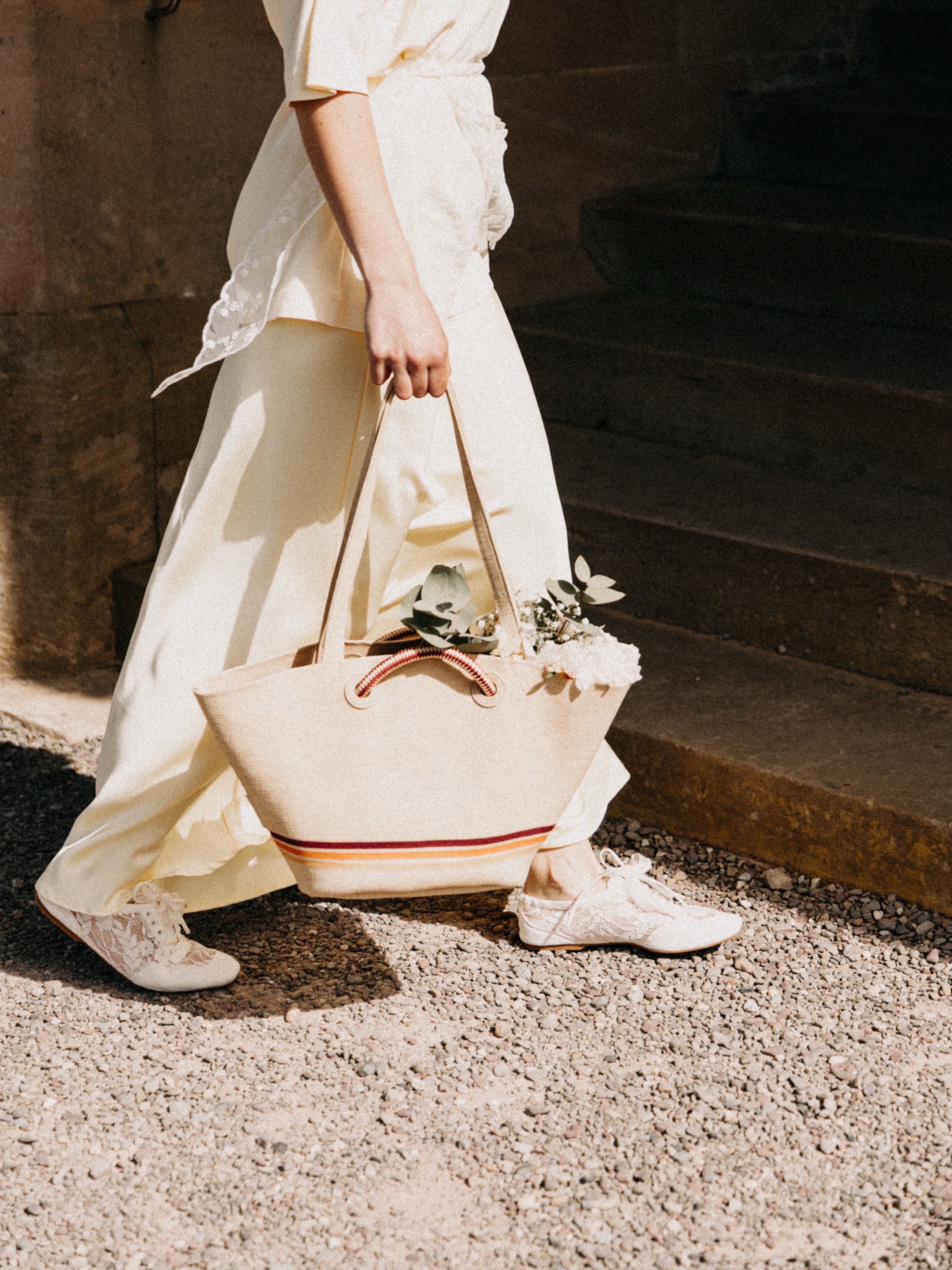Fashionable woman walking outdoors with a beige tote bag and floral decor. Elegant style and summer vibe.