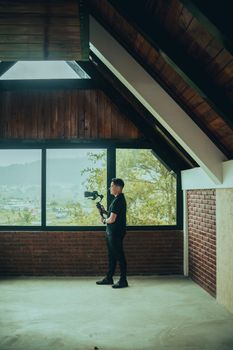 A person holding a camera gimbal in a wooden attic space with city views.