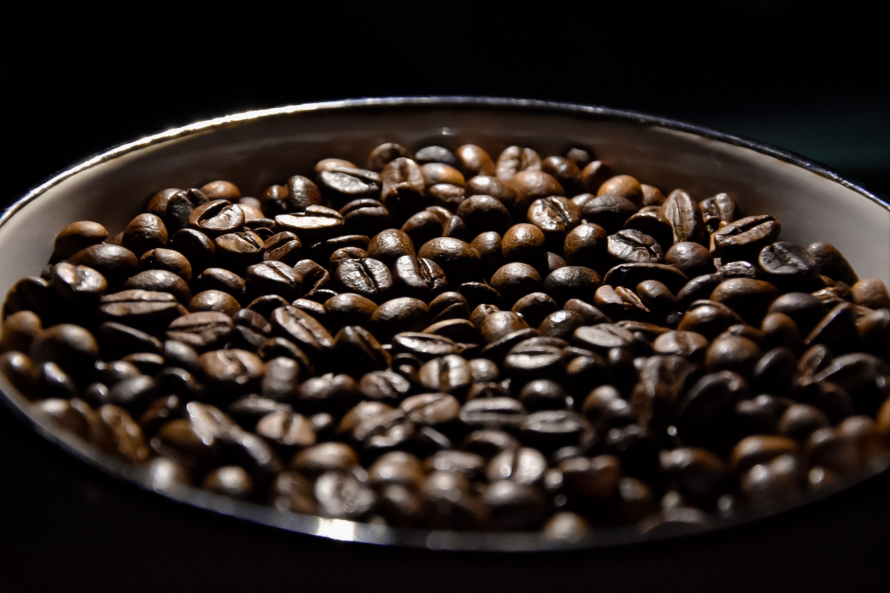 A detailed view of roasted coffee beans in a bowl under dramatic lighting, showcasing texture and richness.