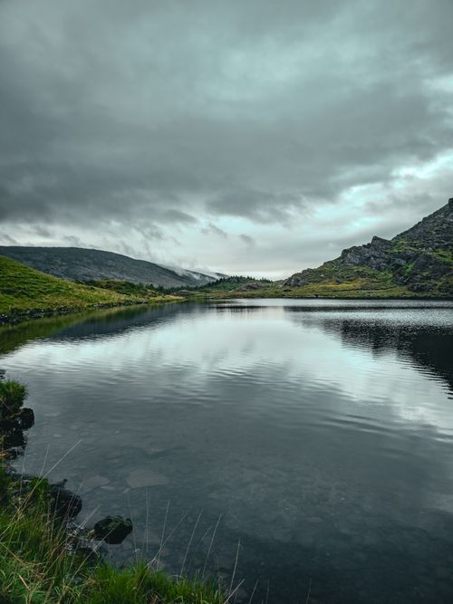 Free Peaceful lake in Ireland surrounded by hills under a moody sky, perfect for nature and travel themes. Stock Photo