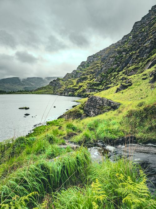 Free Breathtaking view of a lush green lakeside and rocky mountainside in Ireland's countryside. Stock Photo