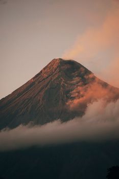 A stunning view of Mayon Volcano in the Philippines, wrapped in clouds and bathed in warm sunset hues.