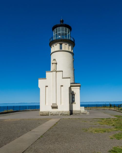 Free A stunning white lighthouse stands tall against a clear blue sky and serene ocean backdrop. Stock Photo