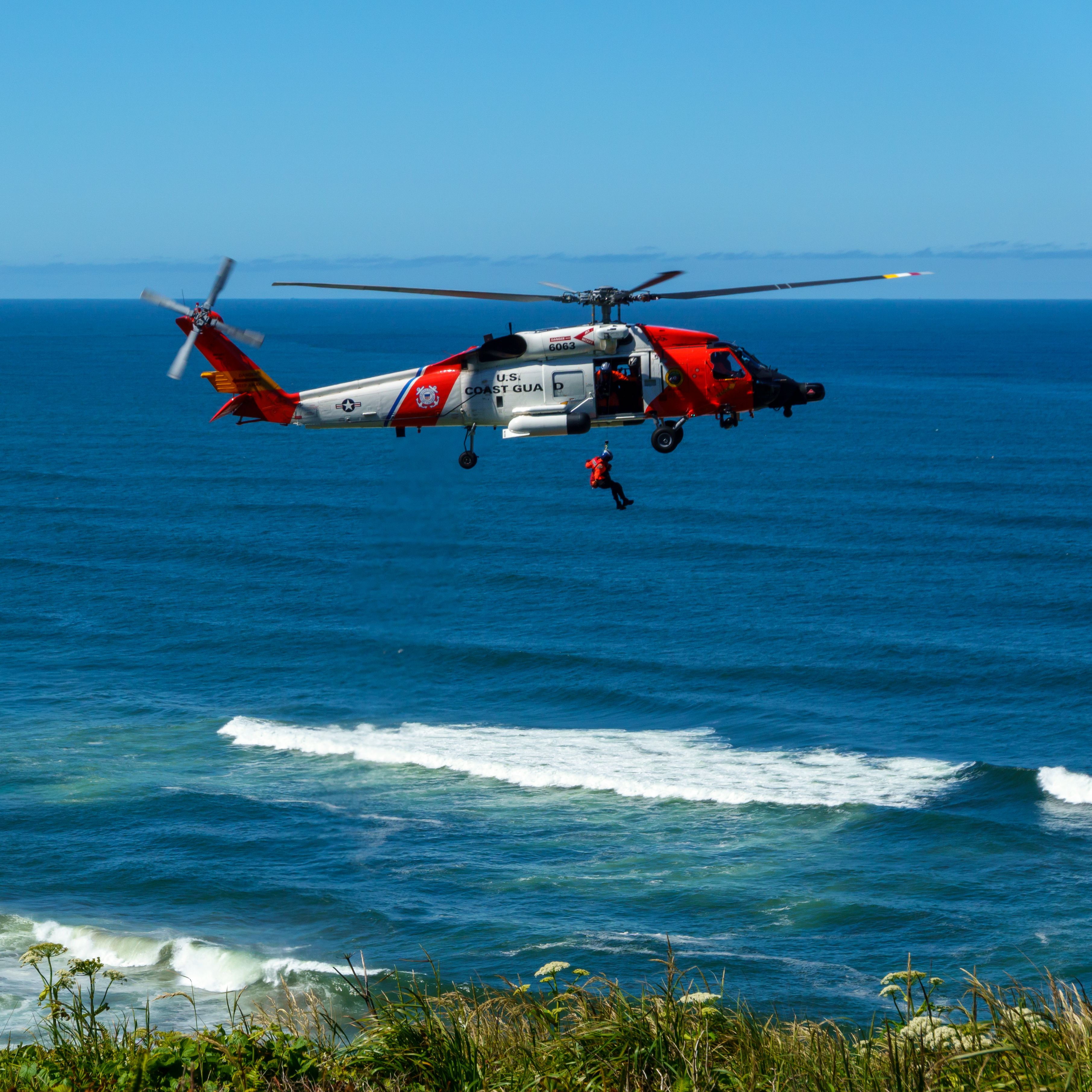 Dramatic US Coast Guard helicopter rescue mission over ocean waves, showcasing teamwork.