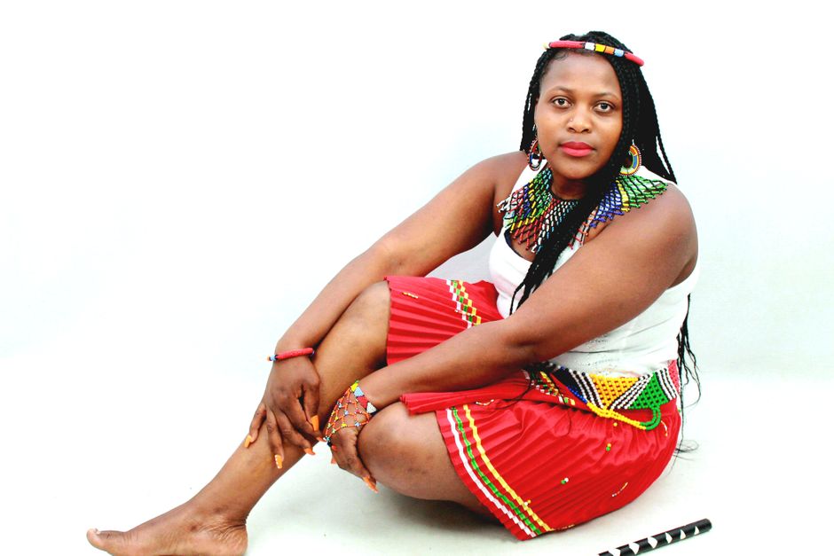 African woman sitting in traditional South African attire with colorful beads in a studio.