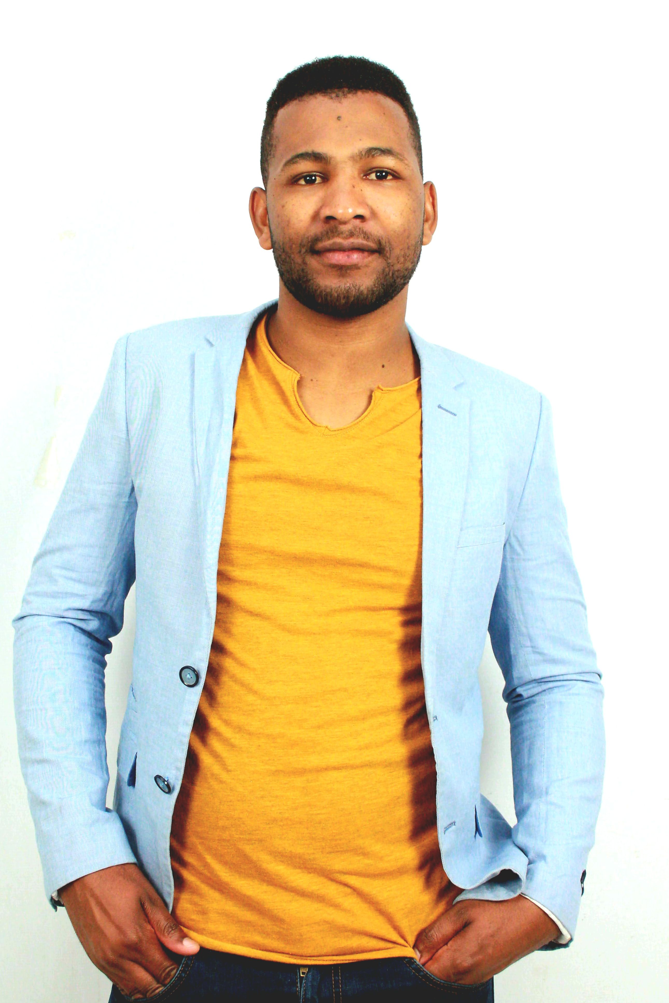 Portrait of a confident man in a light blue blazer and yellow shirt.