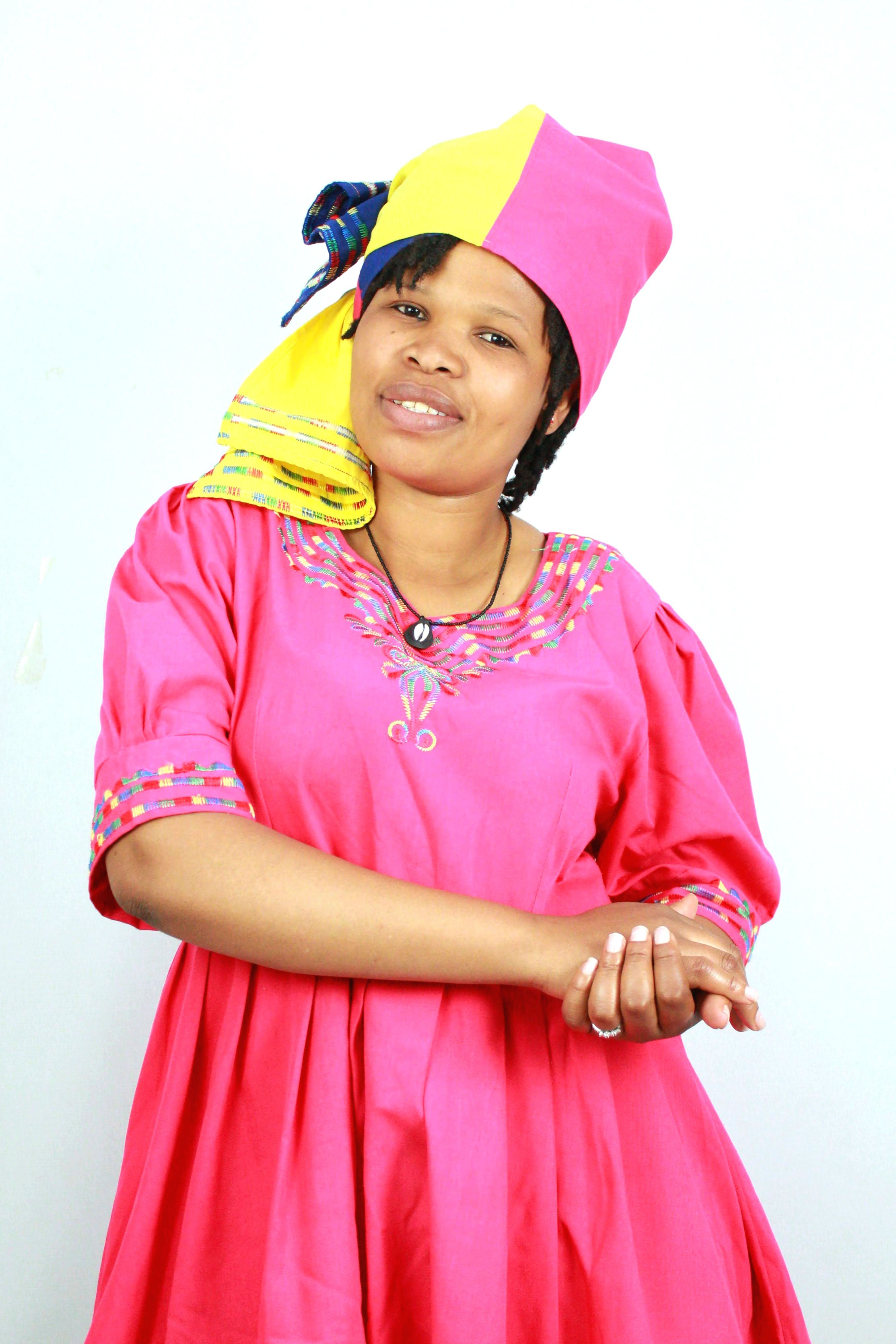 Woman in bright traditional South African dress and headscarf, smiling.