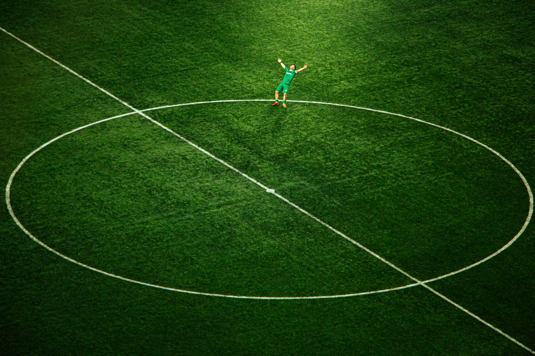 Footballer celebrating alone on a green pitch, aerial view