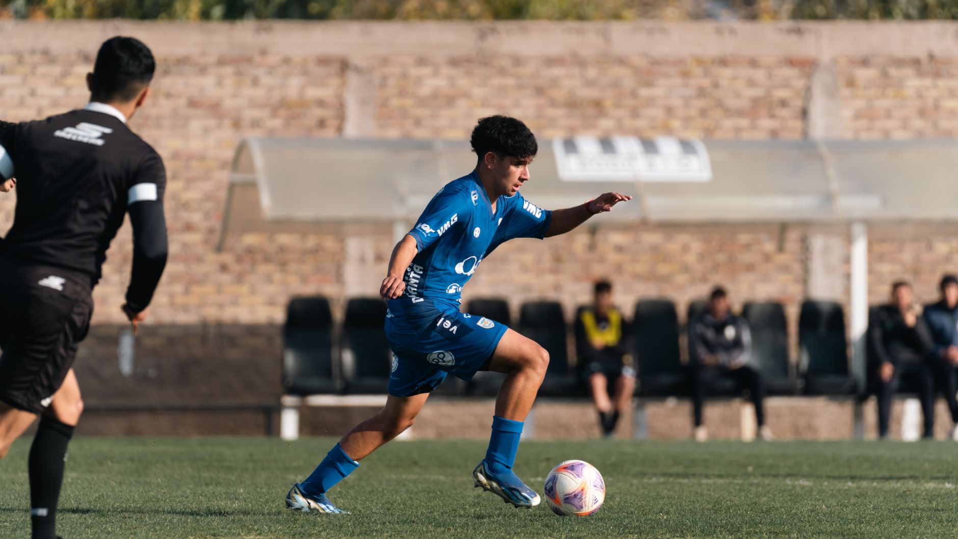 Soccer player in blue uniform dribbles ball during intense outdoor match.