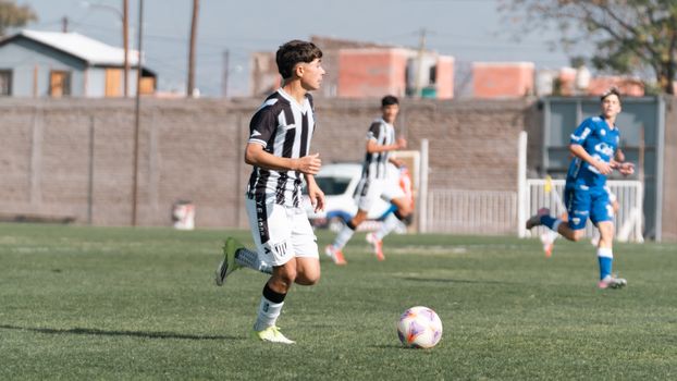Teenage soccer players in action during a match on an outdoor field under daylight.