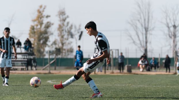 Teen soccer player kicks a ball during a match on an outdoor field.