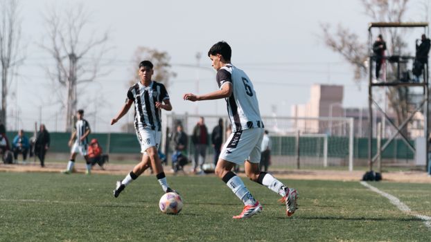 Two young athletes competing in an outdoor soccer match on a sunny day.