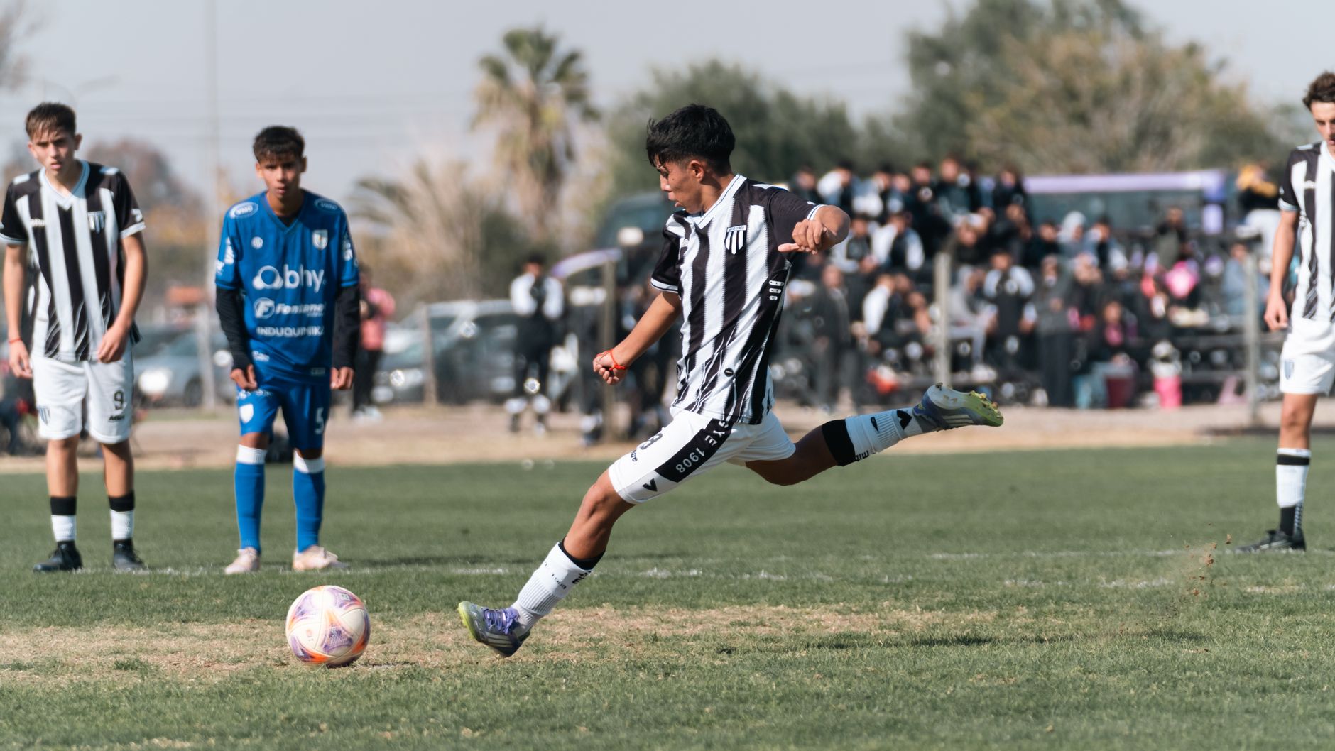 A youth football player performing close-control dribbling drills beside cones on a bright outdoor training pitch