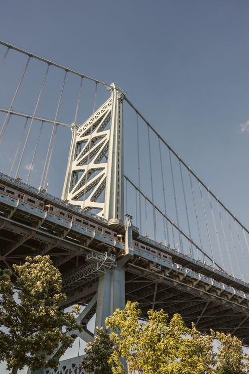 Free View of the Ben Franklin Bridge from below with clear skies and surrounding foliage. Stock Photo