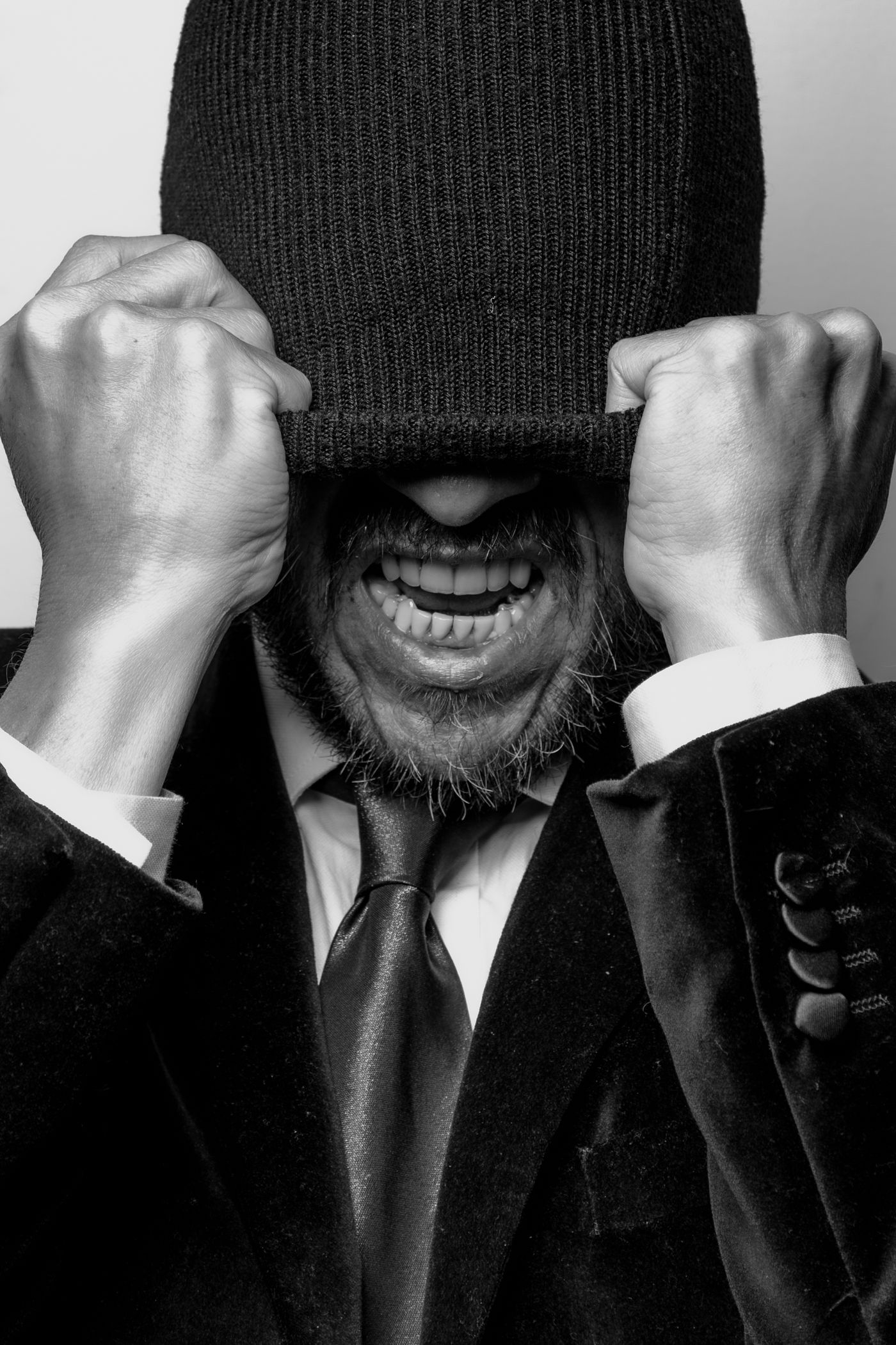 Black and white portrait of a man, eyes closed, hands raised to his head, expression tense