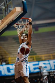 Dynamic action shot of a basketball player dunking during a game in an indoor arena.