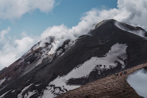 Free A group of hikers trekking on Mount Etna's smoky volcanic summit with snow patches. Stock Photo