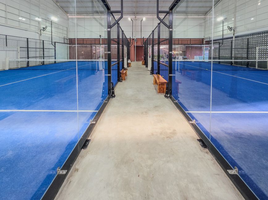 Modern indoor padel tennis courts featuring bright blue surfaces and glass partitions.