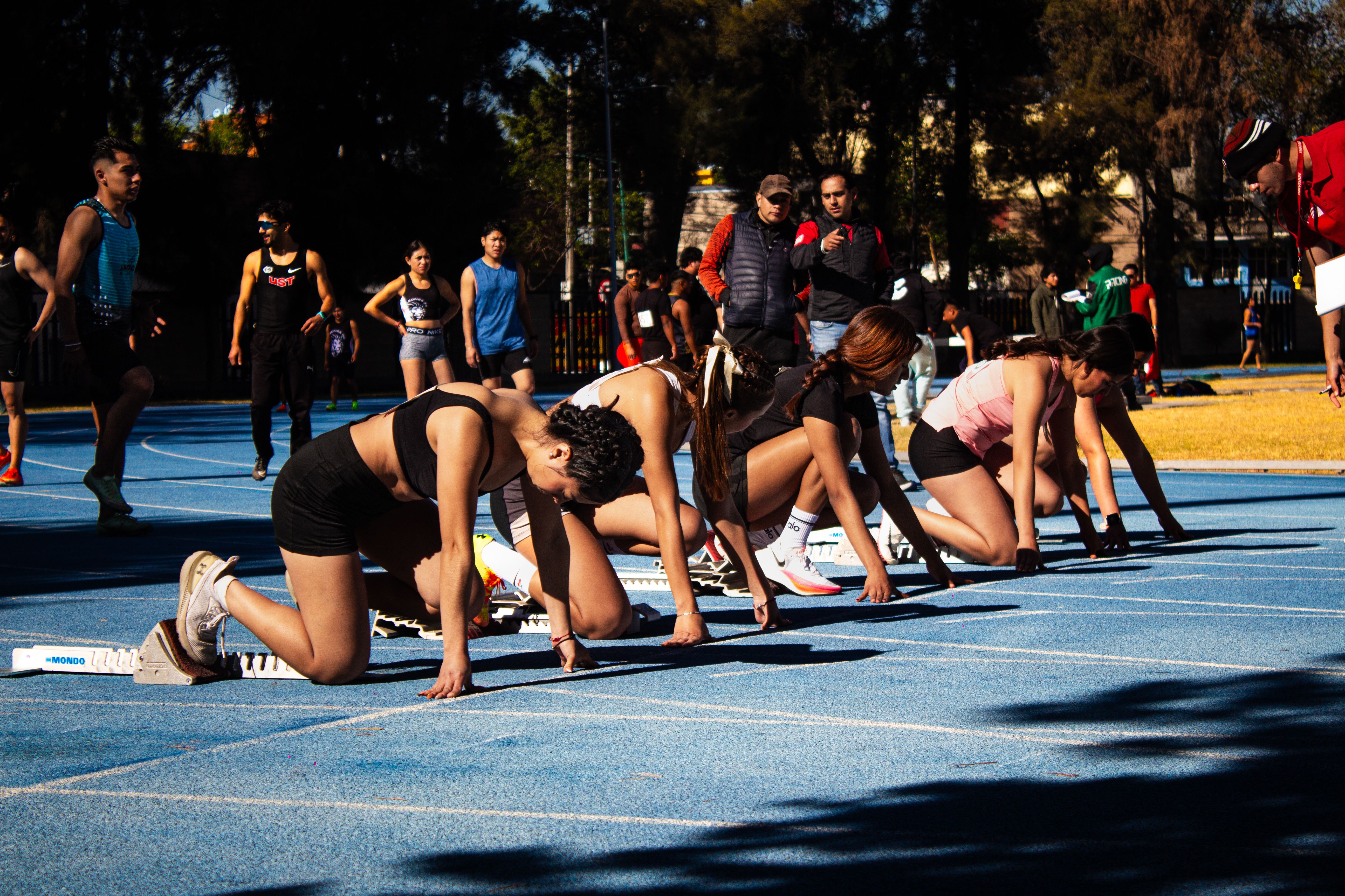 Des athlètes concentrés sur la ligne de départ d'une piste d'athlétisme en extérieur.