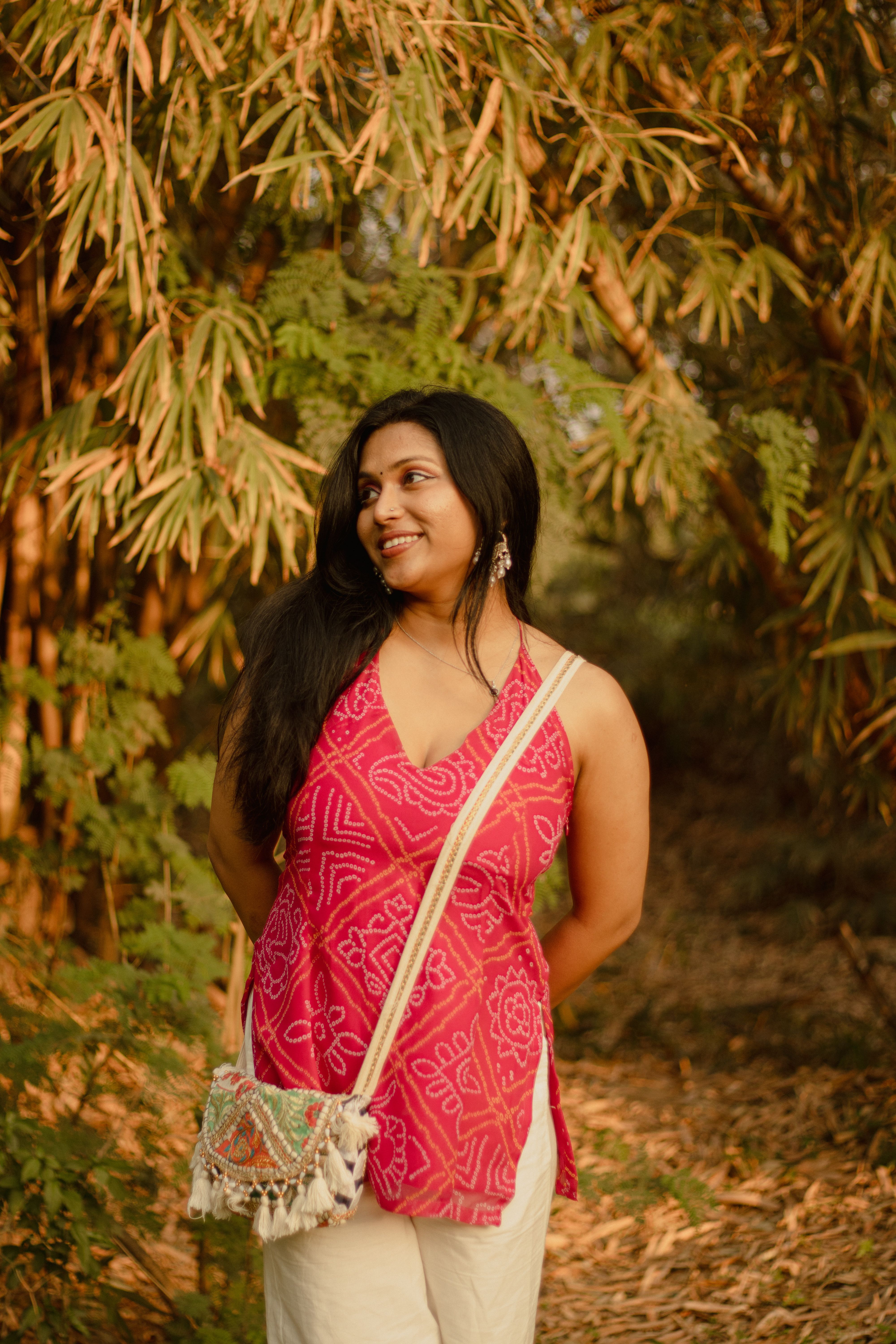 [ColoSach]-cheerful-woman-standing-in-a-bamboo-grove,-wearing-a-vibrant-pink-top-and-carrying-a-bag.