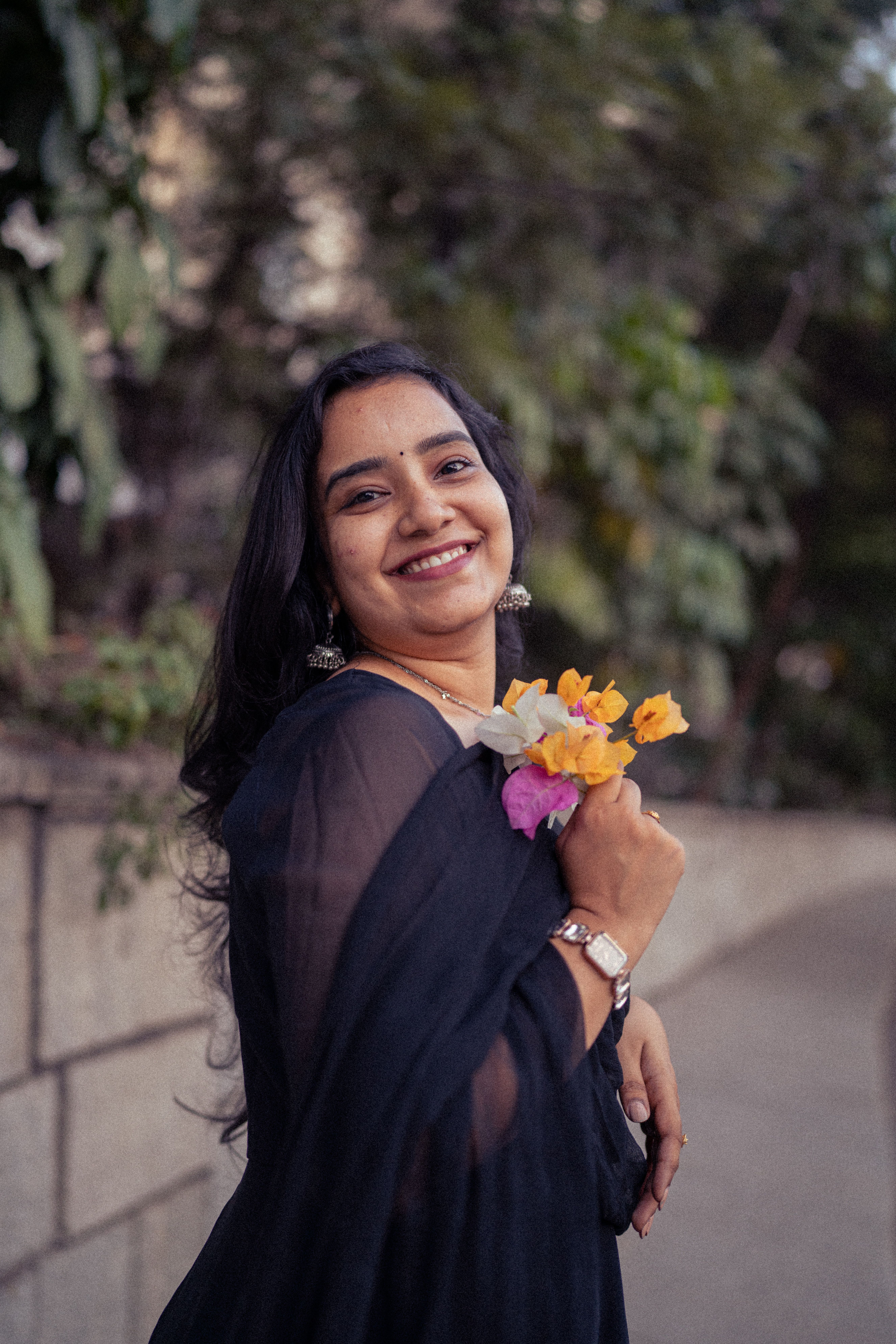 A young woman smiles warmly while holding a bouquet of colorful flowers outdoors.