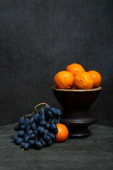 Artistic still life of oranges and grapes on a dark backdrop emphasizing contrast and mood.