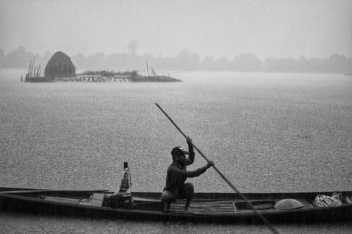 Free A lone fisherman rows his boat amidst rainy weather on a lake. Captured in black and white. Stock Photo