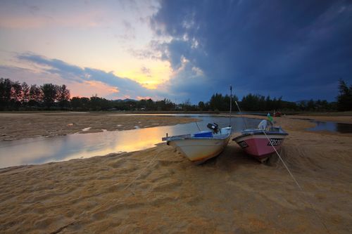 Free Two boats rest on a sandy shore at sunset, with vibrant skies and calm water. Stock Photo