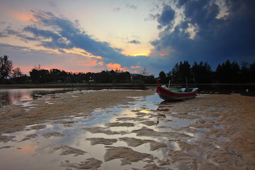 黎明时分，宁静的海滩上，一艘小船停在潮湿的沙滩上，倒映着五彩缤纷的天空