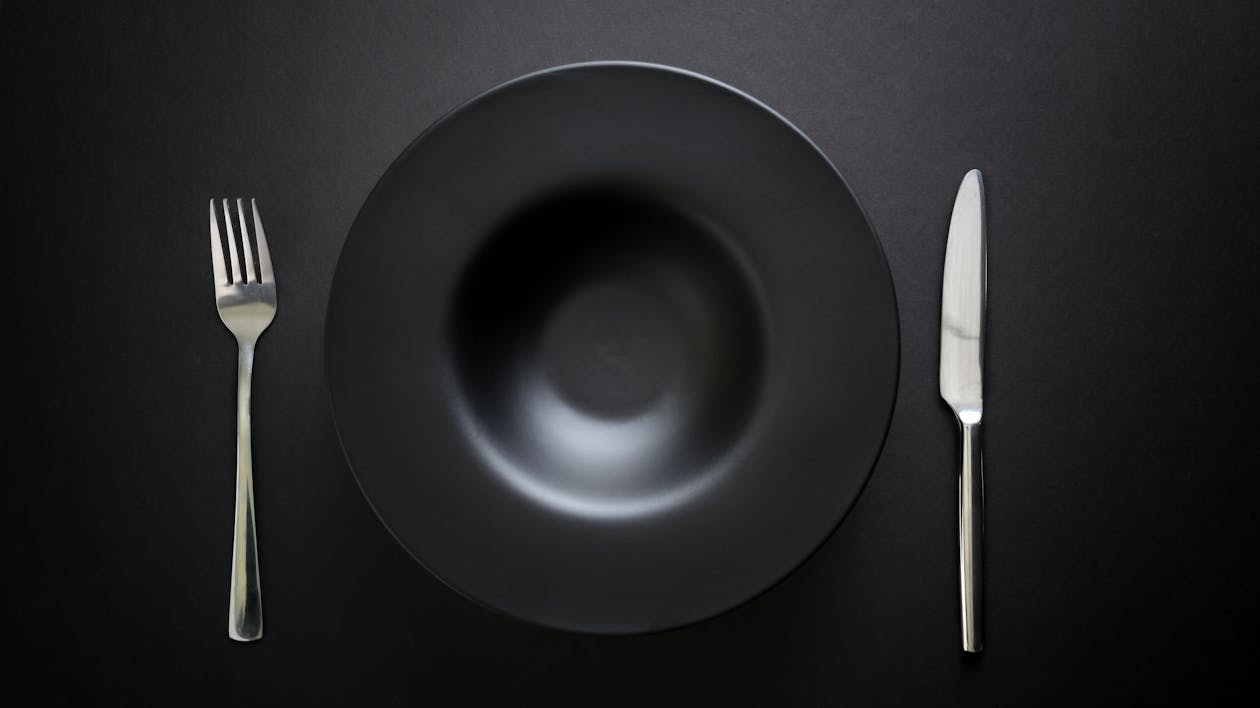 Photo of Black Plate Near Knife and Fork on Black Table