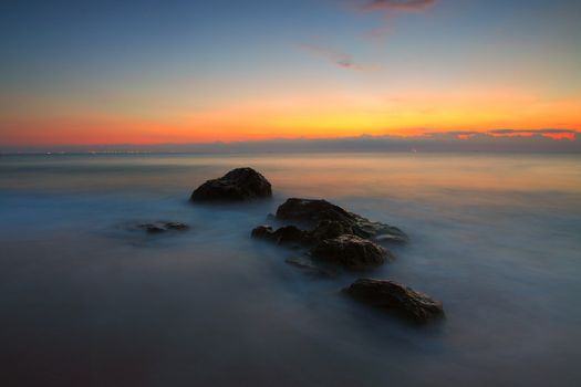 Peaceful sunset over a rocky seashore with gentle waves and colorful sky.