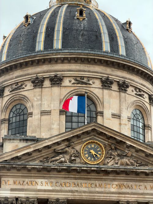 Free The majestic dome of the Institute of France in Paris adorned by the French flag under a cloudy sky. Stock Photo